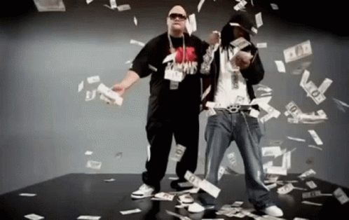 Two Men Are Standing In Front Of A Pile Of Money And One Of Them Is Wearing A Shirt That Says ' Famous ' On It GIF