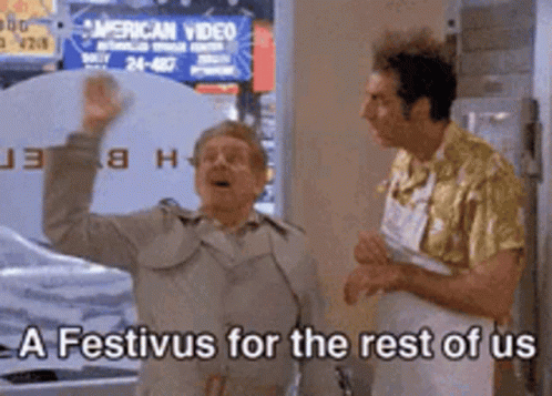 Two Men Are Standing In Front Of A Sign That Says A Festivus For The Rest Of Us . GIF