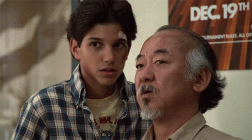 Two Men Are Standing In Front Of A Sign That Says Dec 19Th On It GIF