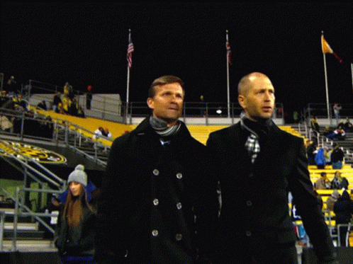 two men are standing in front of a stadium with a yellow sign that says ' t ' on it