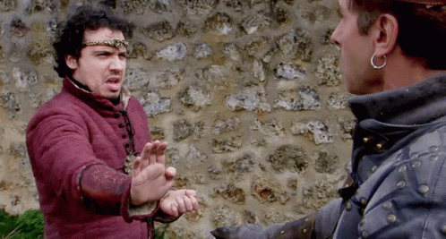 Two Men Are Standing In Front Of A Stone Wall And One Is Wearing A Crown GIF