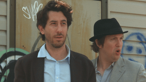Two Men Are Standing In Front Of A Wall With Graffiti On It That Says Swag GIF