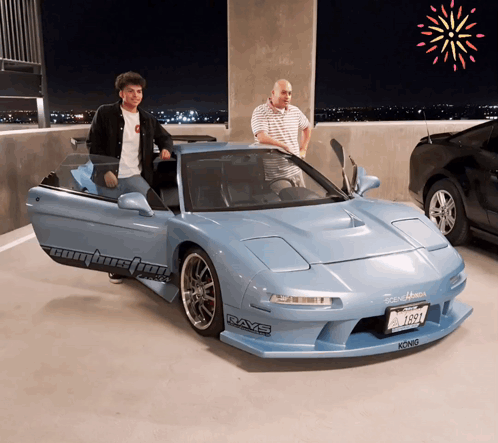 Two Men Are Standing Next To A Blue Sports Car That Says Rays On The Side GIF