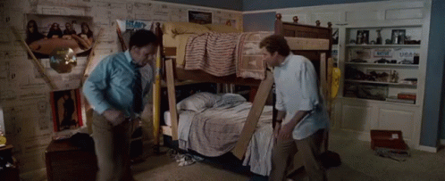 Two Men Are Standing Next To A Bunk Bed In A Room With Posters On The Wall GIF