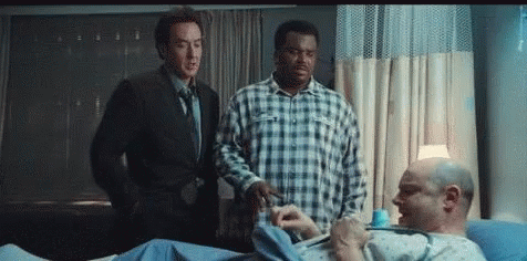 Two Men Are Standing Next To A Man In A Hospital Bed GIF