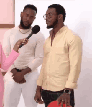 Two Men Are Standing Next To Each Other And A Woman Is Holding A Microphone . One Of The Men Is Wearing Glasses . GIF