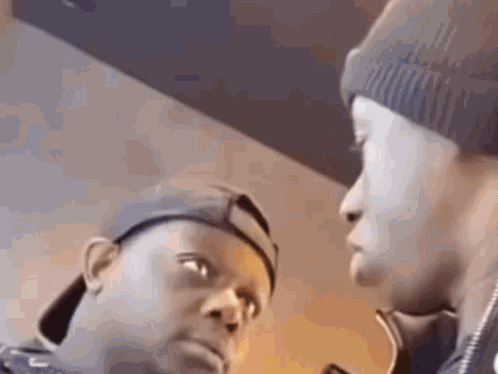 Two Men Are Standing Next To Each Other And Looking At Each Other . One Of The Men Is Wearing A Beanie . GIF
