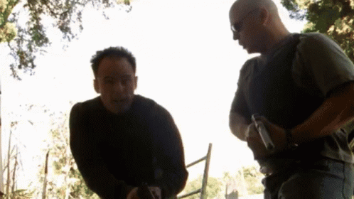 Two Men Are Standing Next To Each Other And One Has A Gun In His Hand GIF