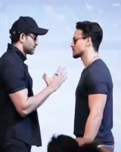 Two Men Are Standing Next To Each Other And Talking To Each Other . One Of The Men Is Wearing A Baseball Cap . GIF