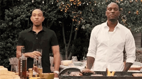 Two Men Are Standing Next To Each Other At A Grill . GIF