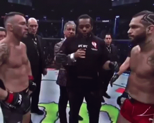 Two Men Are Standing Next To Each Other In A Boxing Ring With A Referee Holding A Microphone . GIF