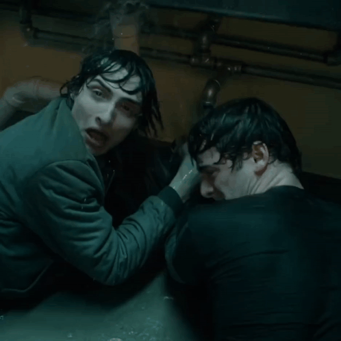 Two Men Are Standing Next To Each Other In A Dark Room And One Is Holding The Other 'S Hand GIF