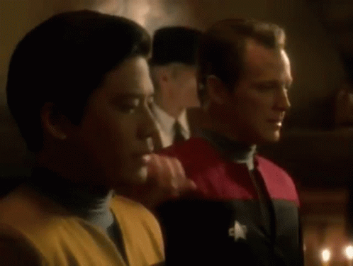 Two Men Are Standing Next To Each Other In A Dark Room . One Of The Men Has A Star On His Uniform . GIF