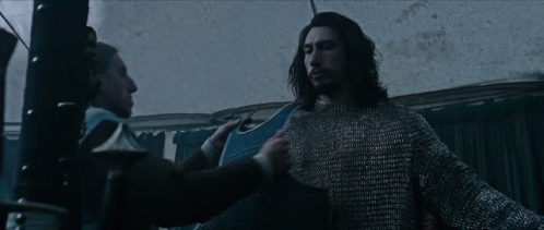Two Men Are Standing Next To Each Other In A Dark Room . One Of The Men Is Wearing A Chain Mail Sweater . GIF