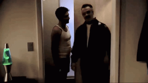 Two Men Are Standing Next To Each Other In A Dark Room With A Green Lava Lamp In The Background . GIF