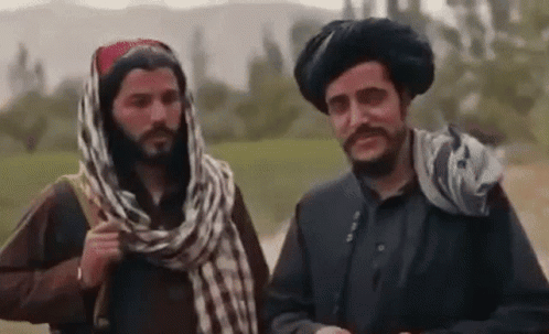 two men are standing next to each other in a field and talking .