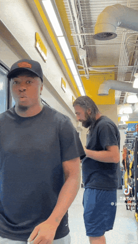 Two Men Are Standing Next To Each Other In A Hallway And One Of Them Has Tiktok Written On His Phone GIF