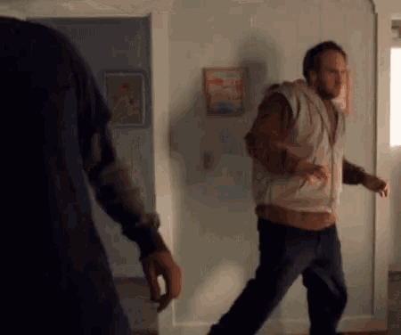 Two Men Are Standing Next To Each Other In A Living Room . One Of The Men Is Wearing A Hoodie . GIF