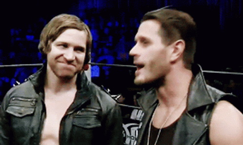 Two Men Are Standing Next To Each Other In A Ring And One Of Them Is Wearing A Leather Vest GIF