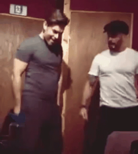 Two Men Are Standing Next To Each Other In A Room . One Of The Men Is Wearing A Hat . GIF