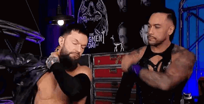 Two Men Are Standing Next To Each Other In A Room . One Of The Men Is Wearing A Leather Jacket . GIF