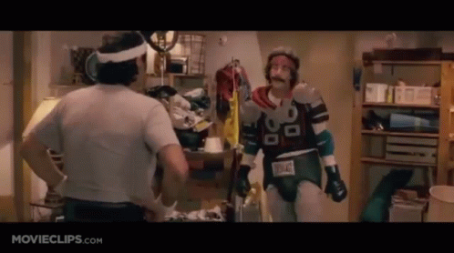 two men are standing next to each other in a room . one of the men is wearing a superhero costume .