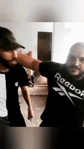 Two Men Are Standing Next To Each Other In A Room Wearing Reebok Shirts . GIF