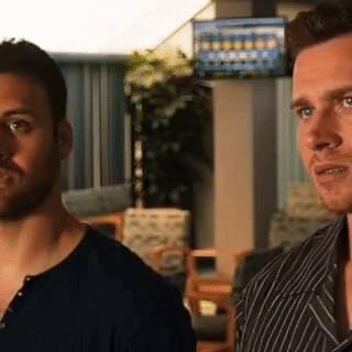 two men are standing next to each other in a room with a tv on the wall