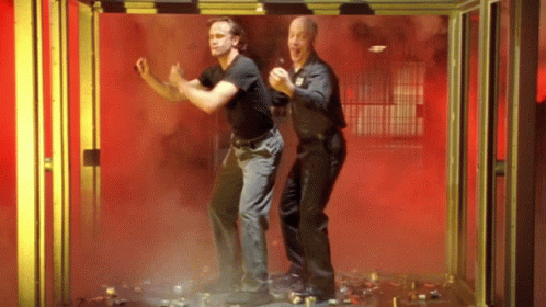 Two Men Are Standing Next To Each Other In A Room With Red Smoke Coming Out Of It . GIF