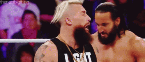 two men are standing next to each other in a wrestling ring . one of the men has a beard .