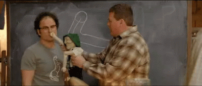 two men are standing next to each other in front of a blackboard . one of the men is holding a stuffed animal .