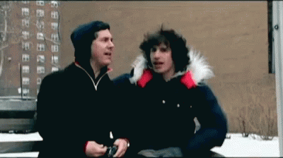 Two Men Are Standing Next To Each Other In Front Of A Building And Talking GIF