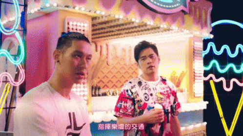 Two Men Are Standing Next To Each Other In Front Of A Carnival Display GIF