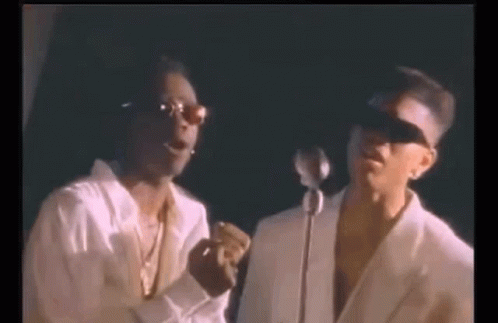 Two Men Are Standing Next To Each Other In Front Of A Microphone And Singing Into It . GIF