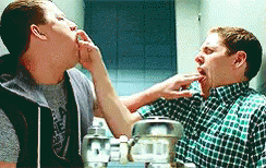 Two Men Are Standing Next To Each Other In Front Of A Mirror And One Of Them Is Licking The Other 'S Face . GIF