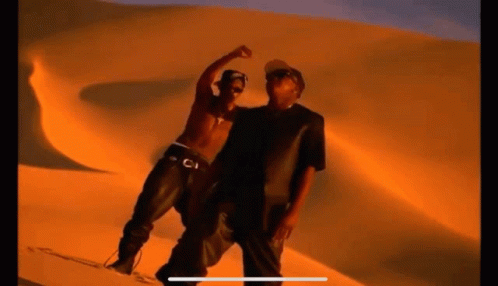 Two Men Are Standing Next To Each Other In Front Of A Sand Dune In The Desert . GIF