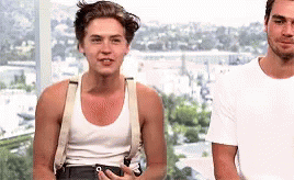 Two Men Are Standing Next To Each Other In Front Of A Window . One Of The Men Is Wearing Suspenders And A Tank Top . GIF