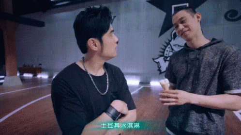 Two Men Are Standing Next To Each Other On A Basketball Court And One Of Them Is Holding An Ice Cream Cone . GIF