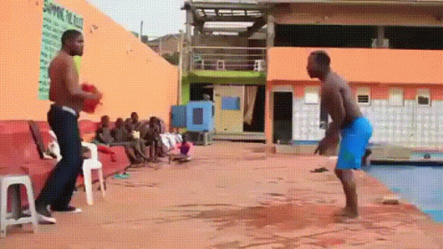 Two Men Are Standing Next To Each Other On A Concrete Surface In Front Of A Pool . GIF