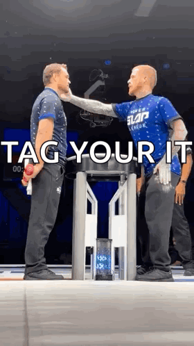 Two Men Are Standing Next To Each Other On A Stage With The Words Tag Your It Written On The Bottom . GIF