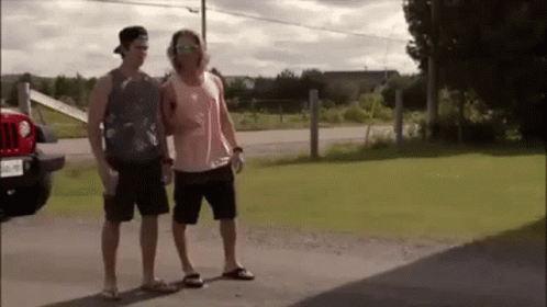 Two Men Are Standing Next To Each Other On The Side Of A Road In Front Of A Jeep . GIF