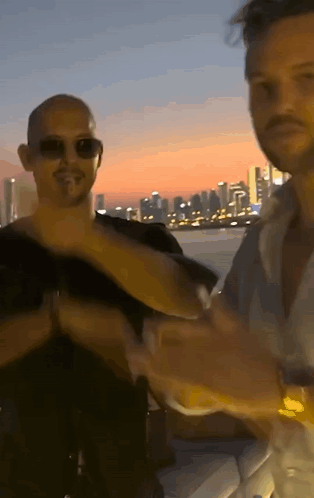 Two Men Are Standing Next To Each Other With A City In The Background GIF