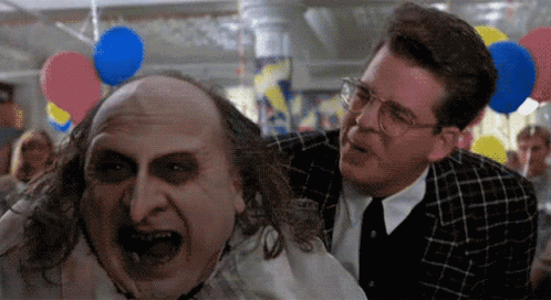 Two Men Are Standing Next To Each Other With Balloons Hanging From The Ceiling In The Background GIF