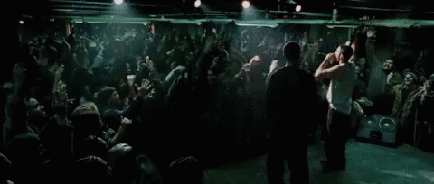 Two Men Are Standing On Stage In Front Of A Crowd Of People GIF