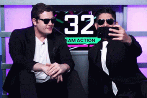 Two Men Are Taking A Selfie In Front Of A Sign That Says 32 GIF
