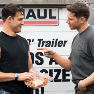 two men are talking in front of a trailer size sign