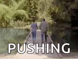 Two Men Are Walking Across A Bridge With The Word Pushing In The Background . GIF