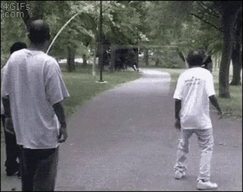 Two Men Are Walking Down A Path In A Park . One Of The Men Is Holding A Bat . GIF