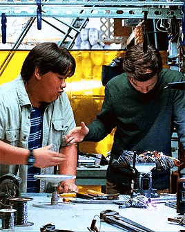 Two Men Are Working On A Project In A Workshop And One Of Them Is Touching Another Man 'S Arm GIF