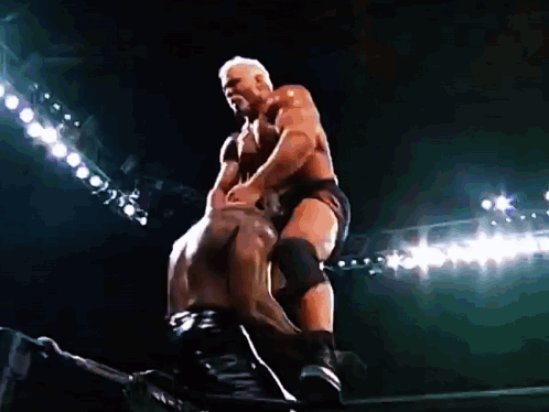 Two Men Are Wrestling In A Dark Stadium With Lights Behind Them . GIF